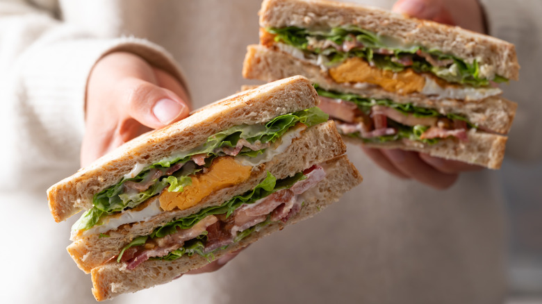 Hands holding out a halved club sandwich.