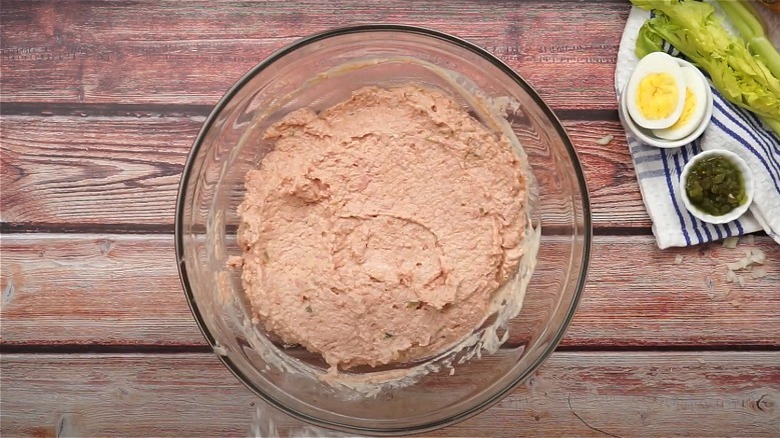 Old-fashioned bologna salad in a glass bowl next to sliced boiled egg, relish, and celery