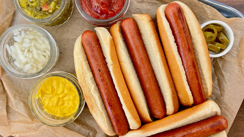 Three grilled hot dogs in buns surrounded by various toppings