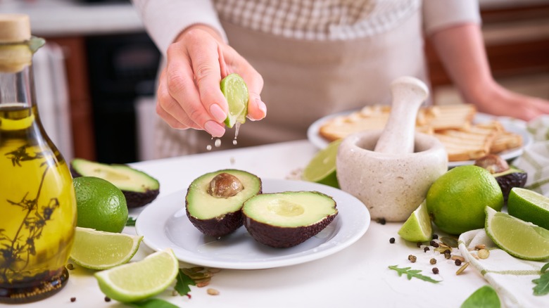 Lime juice being squeezed onto fresh halved avocado