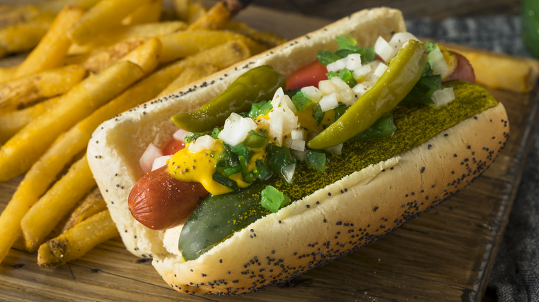 A Chicago-style hot dog sits on a wooden cutting board with fries