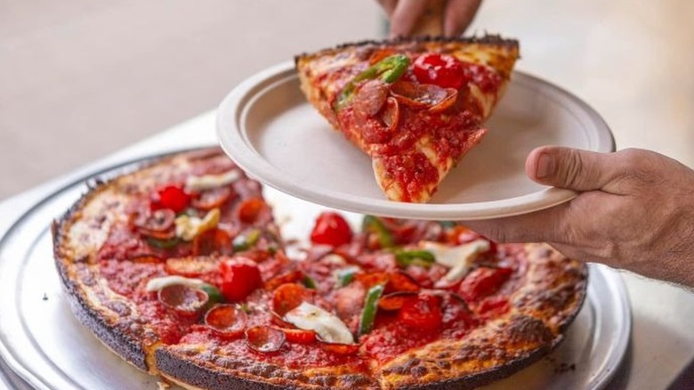 Slice of Milly's pizza being put on a plate over the rest of the pie