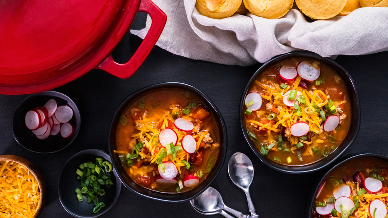 chili in bowls topped with green onions, radishes, cheese, and more