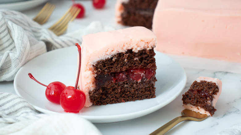 pink-frosted cake on a plate with two maraschino cherries