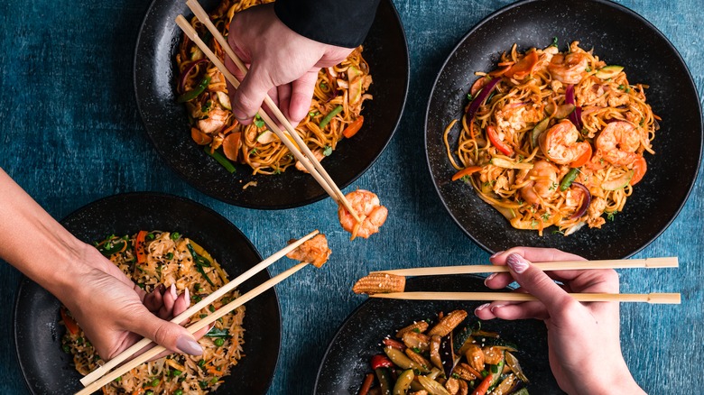 Hands holding chopsticks over plates of food