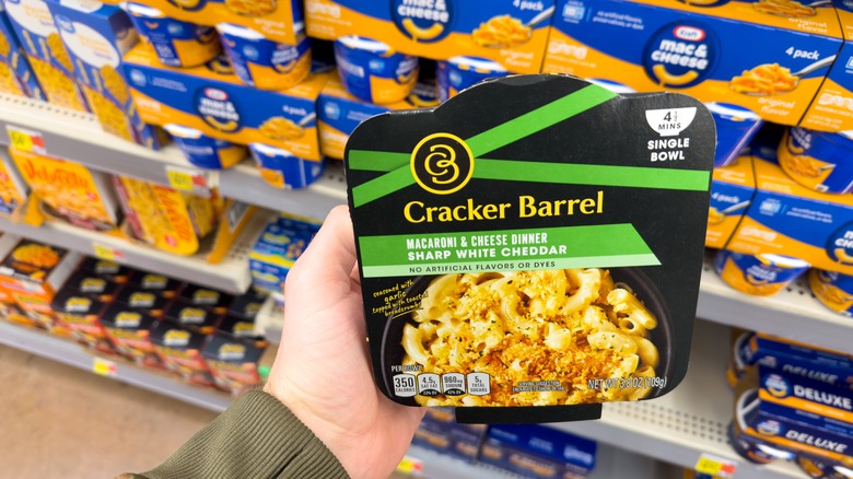 A hand holds a package of Cracker Barrel mac and cheese in a grocery store aisle