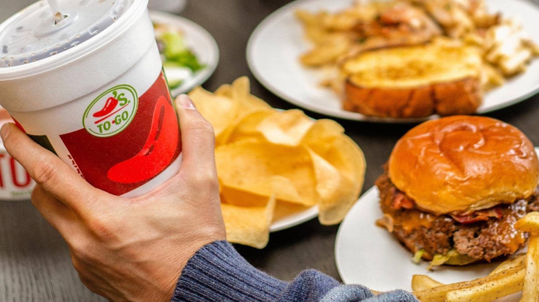 A hand holding a Chili's to-go cup in front of various Chili's menu items