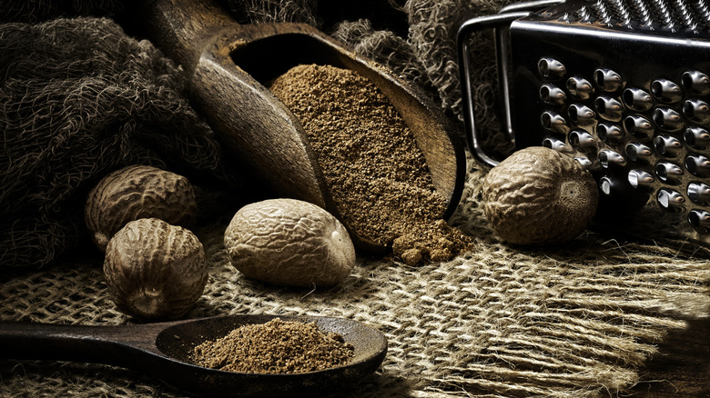 ground nutmeg lies in a scoop next to a whole nutmeg with grater