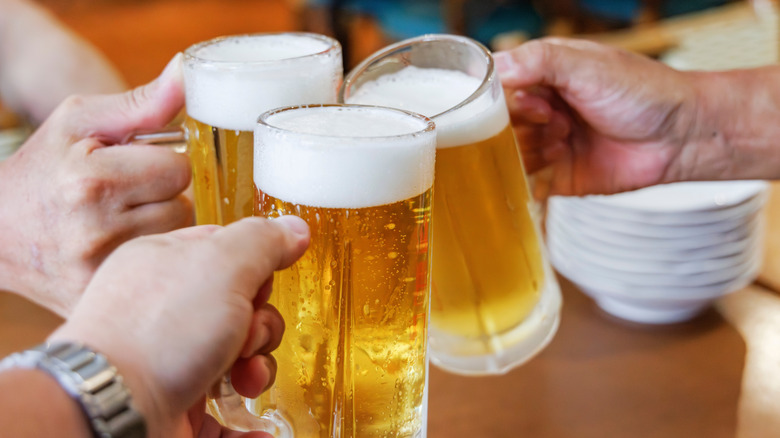 Hands clink beer glasses together.