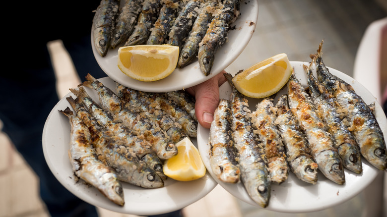 Three plates of whole sardines with spices and lemon wedges