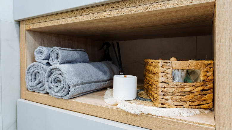 Rolled towels sit cutely in a corner of a shelf next to bathroom goods and a candle