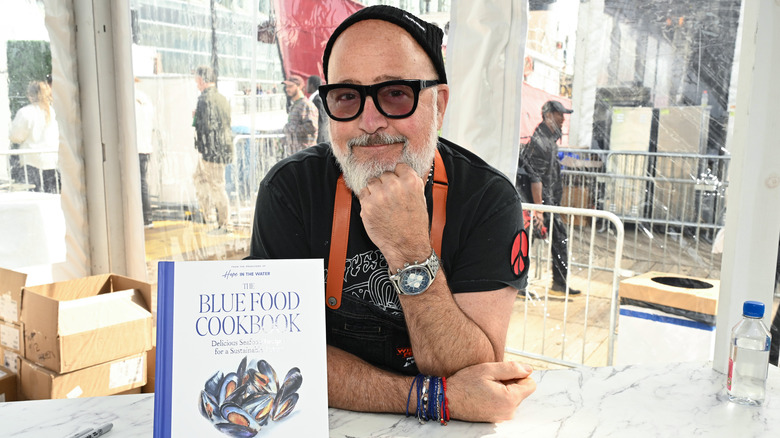 Andrew Zimmern posing next to a cookbook