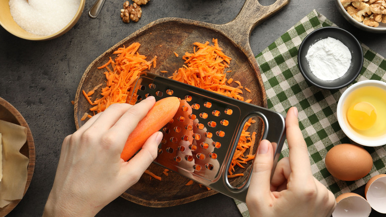 Person grating fresh carrot near carrot cake ingredients