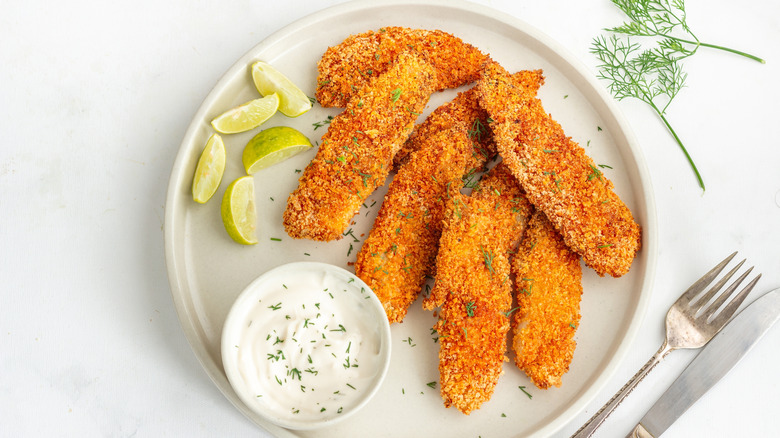 crispy fried fish with lime wedges and tartar sauce on a white plate