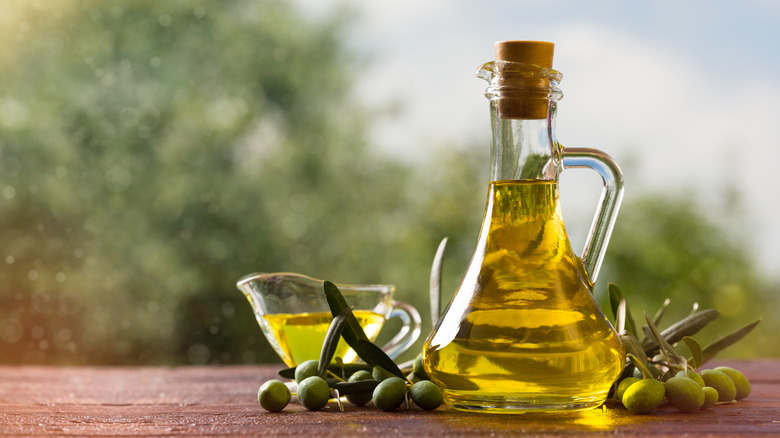 Glass bottle of olive oil surrounded by olives