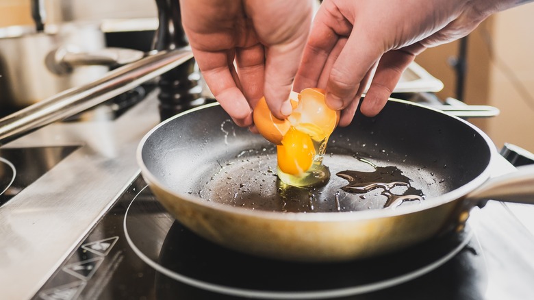 Person cracks egg into pan with oil.