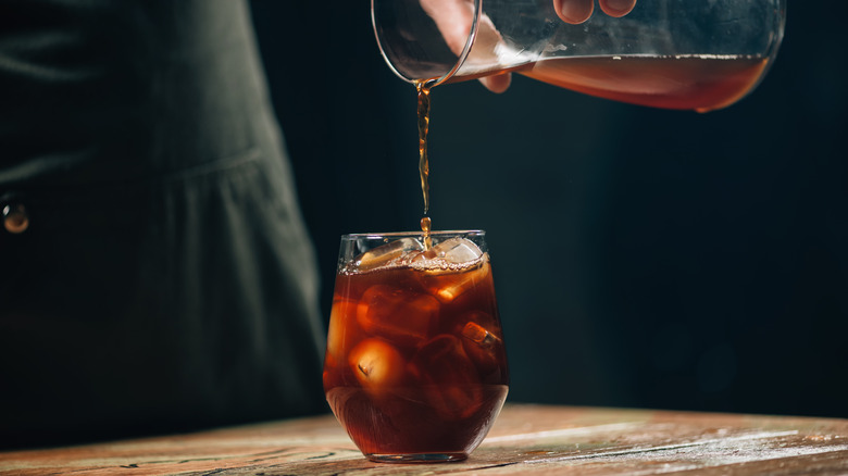 A hand pouring cold brew coffee out of a carafe into a glass with ice