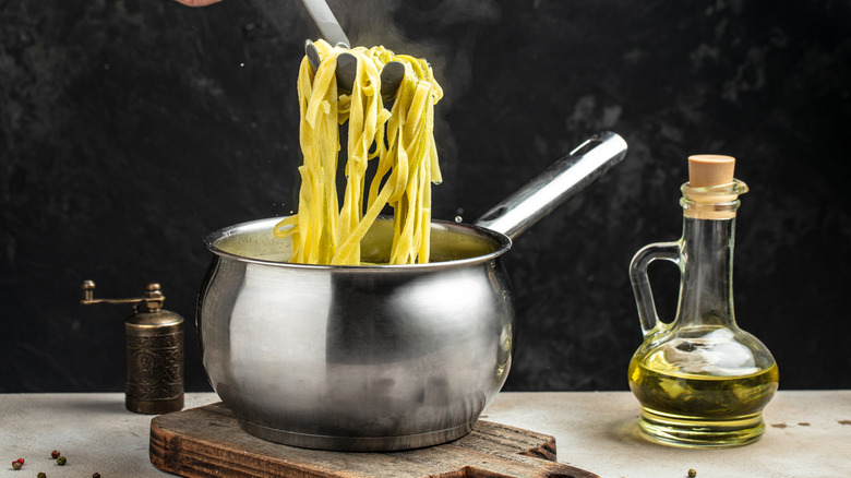 A pasta fork holds up noodles from a pot with a bottle of olive oil next to it