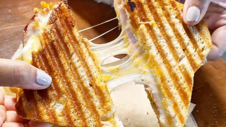 Hands pull apart two halves of a grilled cheese sandwich, with melted cheese stretching between them