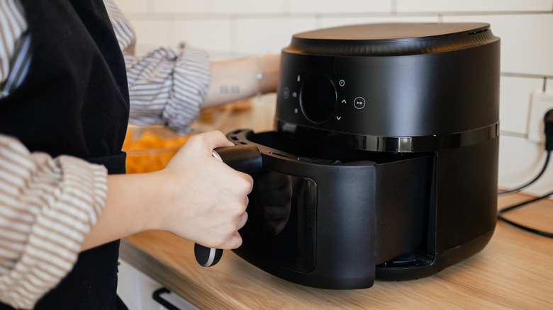A woman holds onto the handle of an air fryer basket