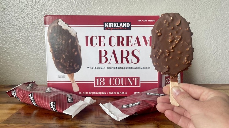 A hand holds a Kirkland Signature Ice Cream Bar in front of its packaging.