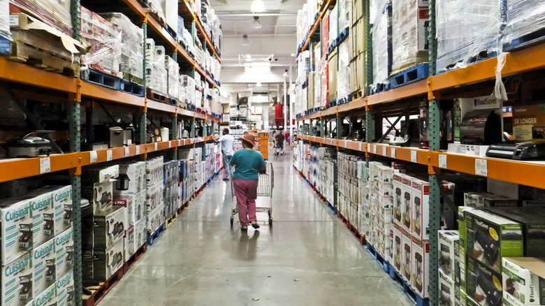 A woman pushes her cart down a wide Costco aisle