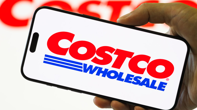 Someone holds a smart phone with the Costco logo blazen across