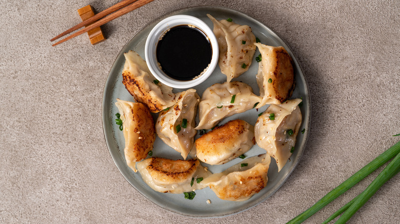 A plate of cooked potstickers surrounding a cup of soy sauce.