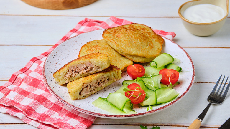 Belarusian potato pancakes, stuffed with minced beef, are served with a salad of cucumber and tomato