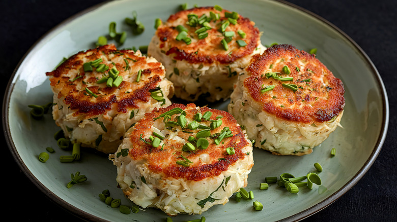 Four browned crab cakes sprinkled with chopped scallions on a plate