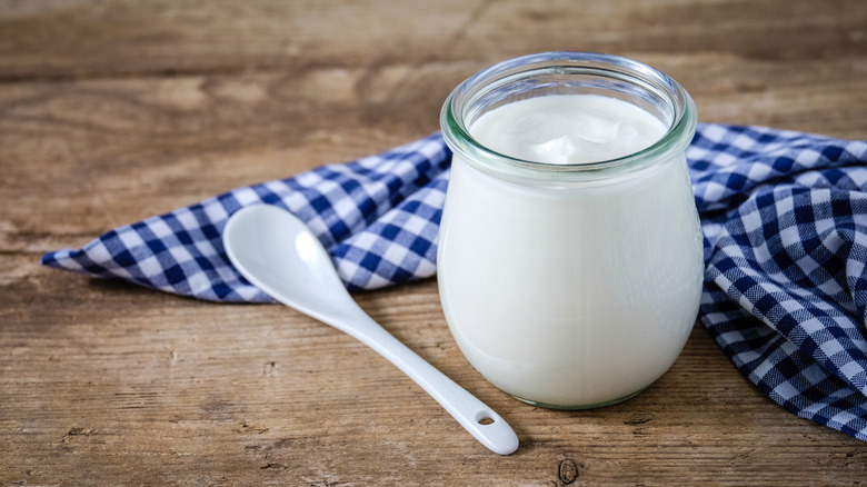 A glass jar of Skyr yogurt sits on a gingham towel with a spoon nearby