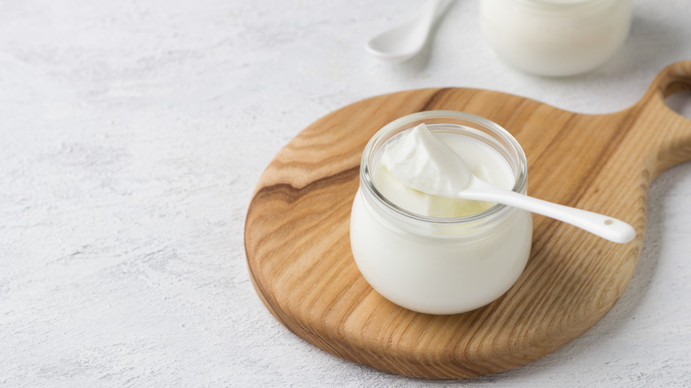 Greek yogurt in a glass jar on a wooden cutting board