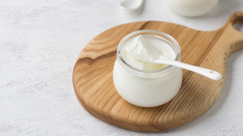 Greek yogurt in a glass jar on a wooden cutting board