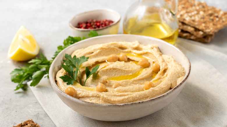 Bowl of hummus surrounded by lemon, olive oil, and crackers