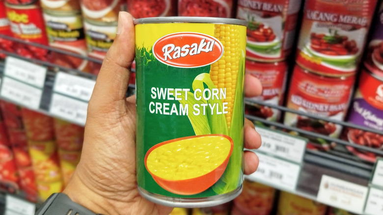 Hand holding a can of creamed corn in grocery store
