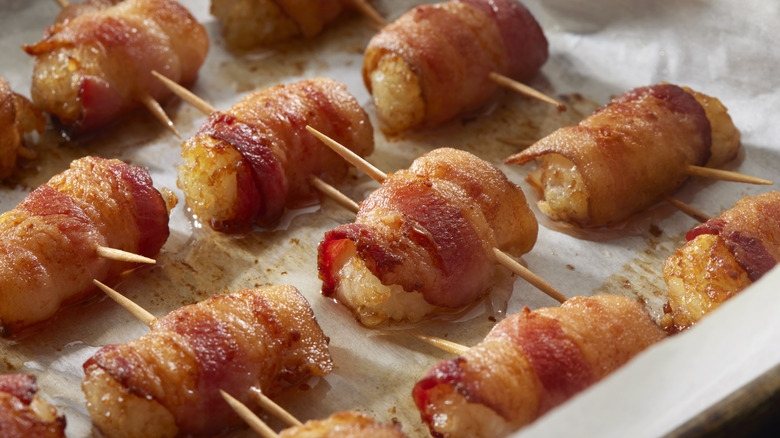 Bacon-wrapped tater tots on a baking sheet secured with toothpicks