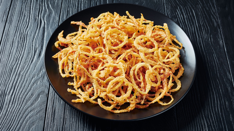 Thin, crispy french fried onions in a round black shallow bowl on a black wooden surface