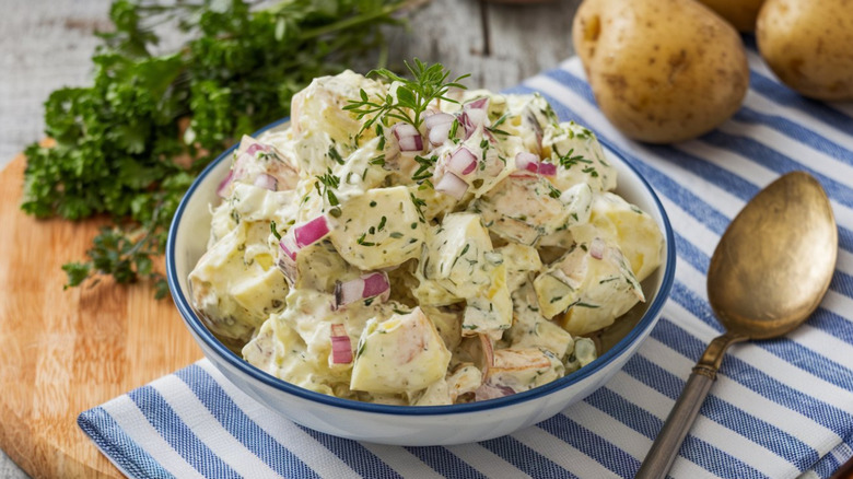Potato salad with chopped red onions and sprinkled green herbs in a blue-rimmed white bowl