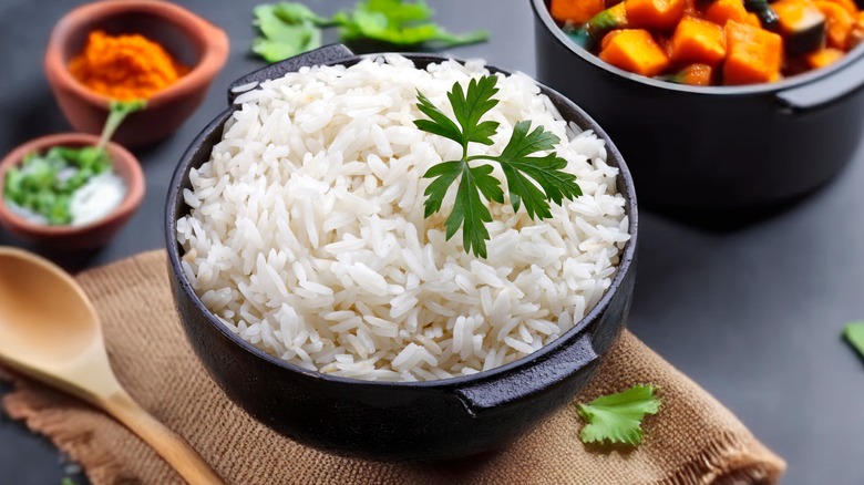 A bowl of white rice topped with parsley next to other ingredients