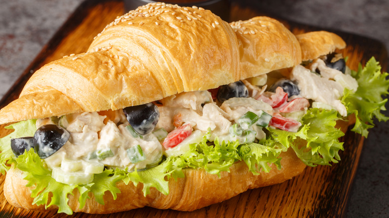 Chicken salad on a croissant on a wooden cutting board.
