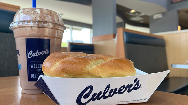 A Culver's burger in a cardboard serving container sits next to a Culver's milkshake on a restaurant table