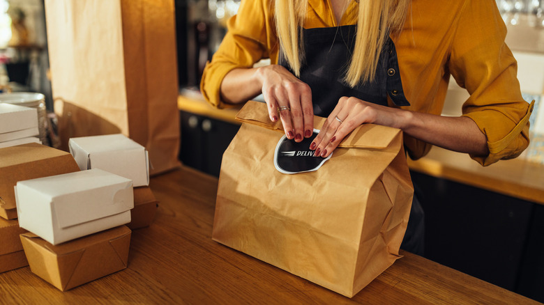 A worker seals a bag of takeout, which sits next to several boxes of takeout.