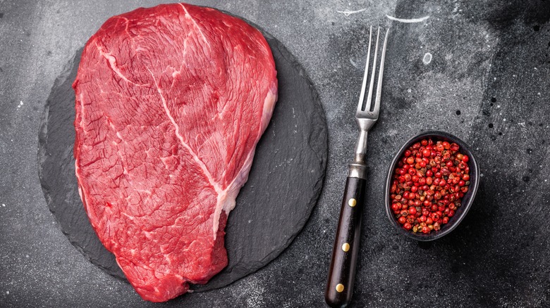 Sirloin steak on a black slate and peppercorns