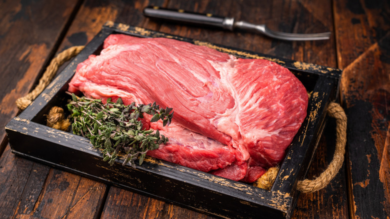 Uncooked top round cut in a box with fresh thyme.