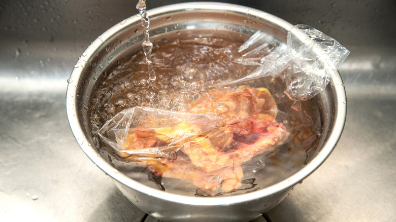 Frozen chicken in a sealed bag in a large bowl of water