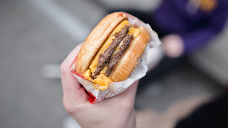 A fast food double-cheeseburger is held in one hand