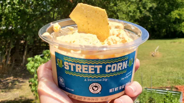 A hand holds up a tub of Aldi Street Corn dip outside