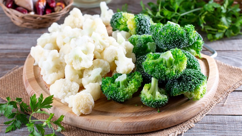 Broccoli and cauliflower florets on a round wood cutting board