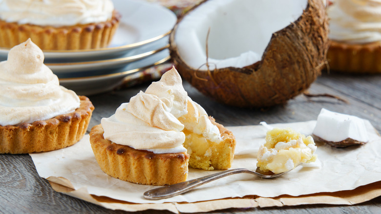 mini coconut custard pies topped with whipped cream or meringue sit beside sliced coconuts