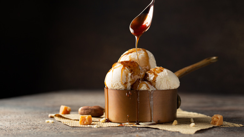 A spoonful of caramel is drizzled onto a scoop of vanilla ice cream